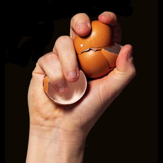 White hand holding up broken eggshells